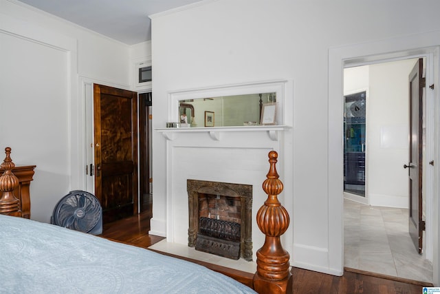 bedroom featuring a fireplace with flush hearth, wood finished floors, baseboards, and crown molding