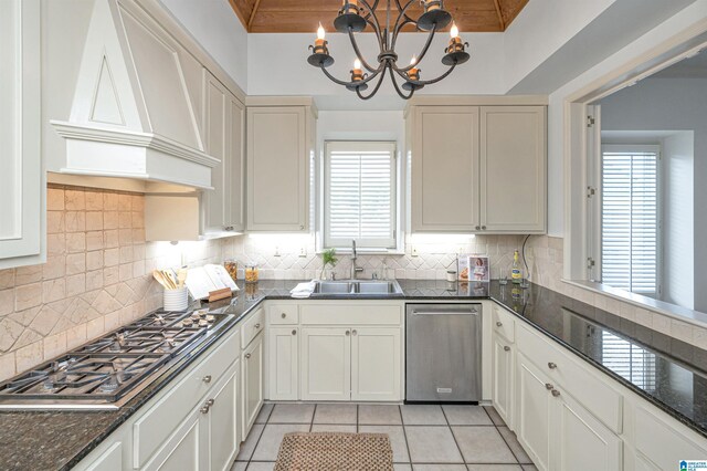 kitchen with light tile patterned floors, custom range hood, appliances with stainless steel finishes, a chandelier, and sink