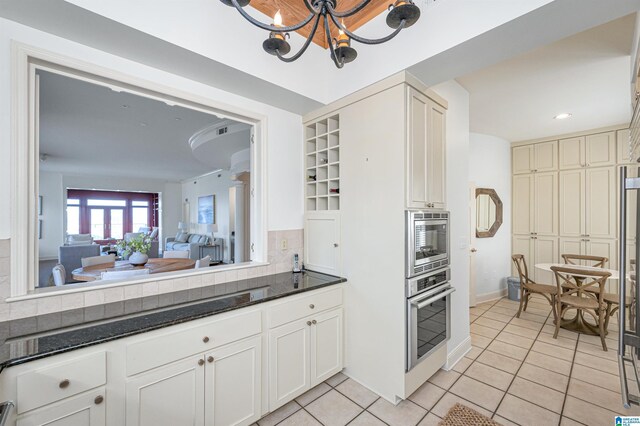 kitchen with a notable chandelier, appliances with stainless steel finishes, decorative backsplash, white cabinetry, and light tile patterned flooring