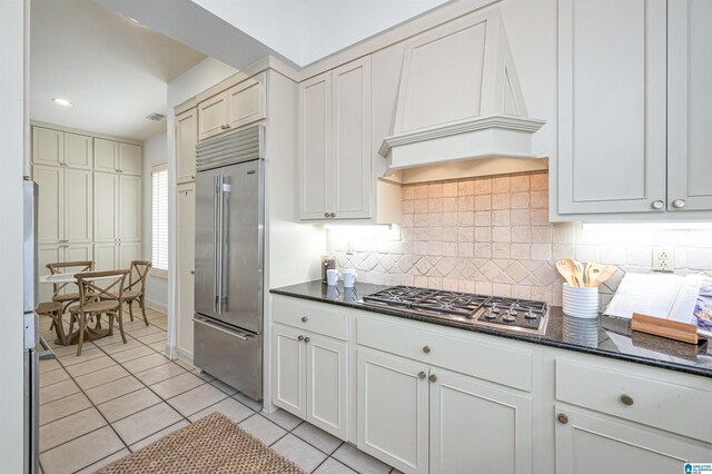 kitchen with custom range hood, light tile patterned floors, tasteful backsplash, stainless steel appliances, and white cabinets