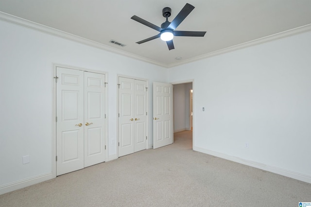 unfurnished bedroom featuring two closets, ceiling fan, light colored carpet, and crown molding