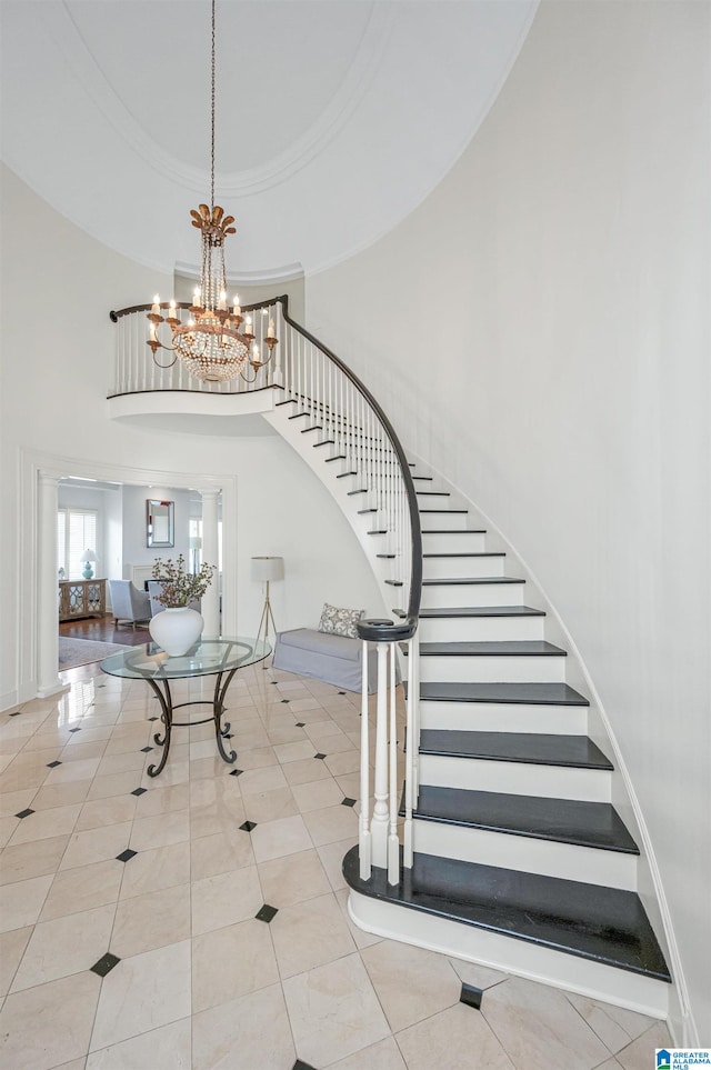 stairs featuring crown molding, a towering ceiling, tile patterned floors, and an inviting chandelier