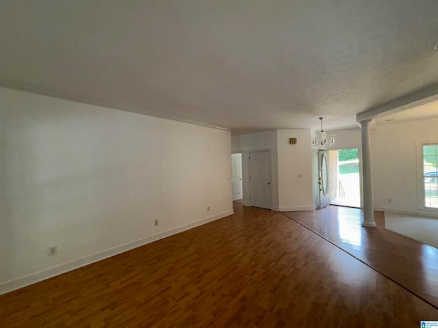 unfurnished living room with an inviting chandelier, decorative columns, and hardwood / wood-style flooring