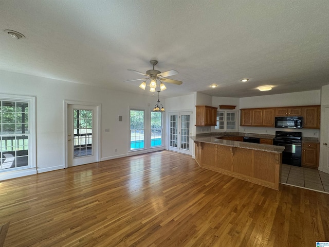 kitchen with a peninsula, light wood-type flooring, brown cabinetry, and black appliances