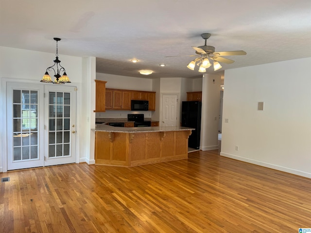 kitchen featuring light wood-type flooring, ceiling fan with notable chandelier, kitchen peninsula, and black appliances