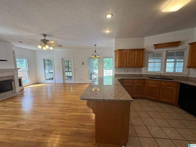 kitchen featuring a healthy amount of sunlight, ceiling fan with notable chandelier, a tiled fireplace, and light hardwood / wood-style flooring