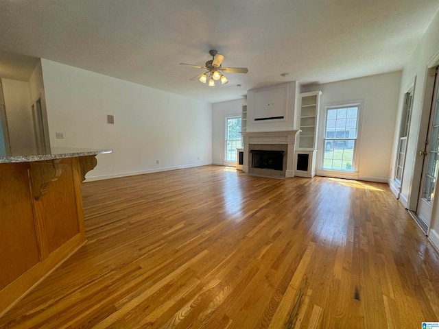 unfurnished living room with a wealth of natural light, a tiled fireplace, ceiling fan, and light wood-type flooring