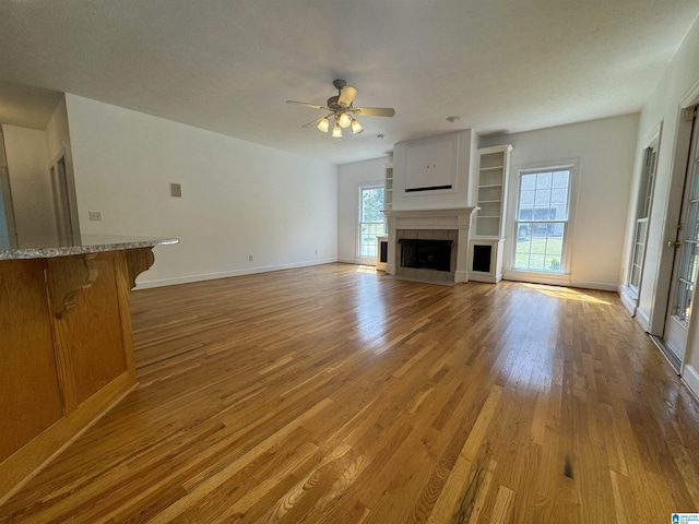 unfurnished living room with a tiled fireplace, baseboards, a ceiling fan, and light wood-style flooring