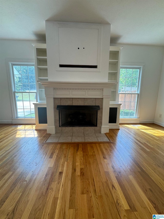 unfurnished living room with light wood-type flooring, a fireplace, plenty of natural light, and a textured ceiling