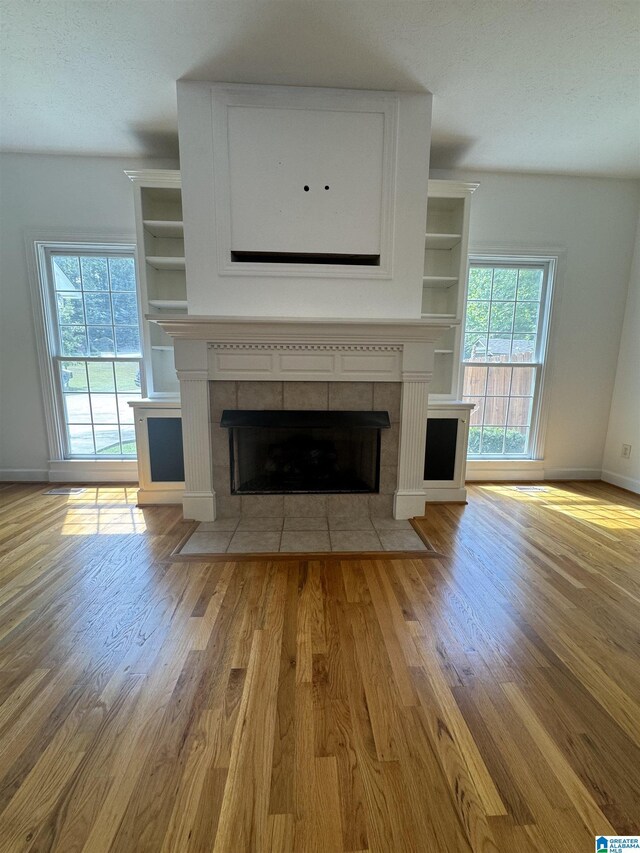 unfurnished living room with baseboards, a tiled fireplace, and wood finished floors