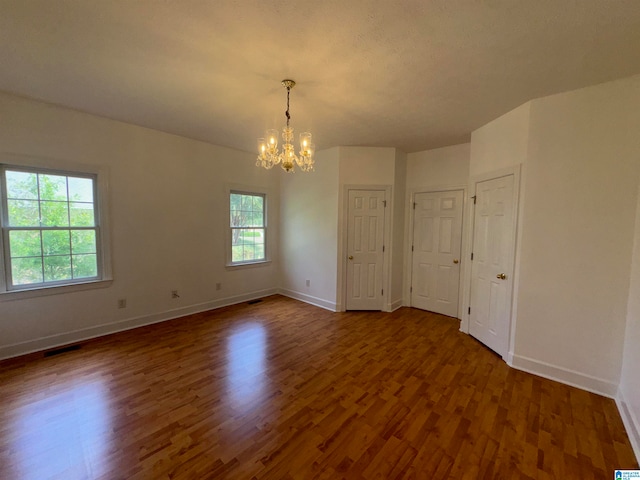 empty room with a notable chandelier and dark wood-type flooring