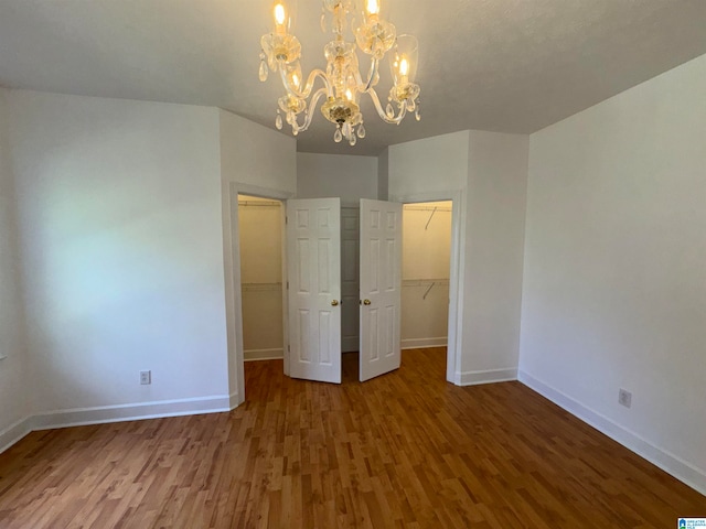 unfurnished bedroom with an inviting chandelier, a closet, a walk in closet, and hardwood / wood-style floors