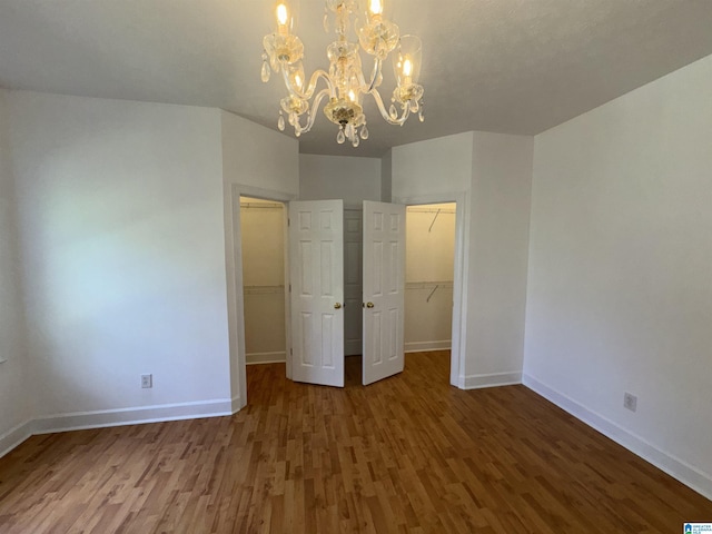 unfurnished bedroom with a spacious closet, baseboards, a chandelier, and wood finished floors