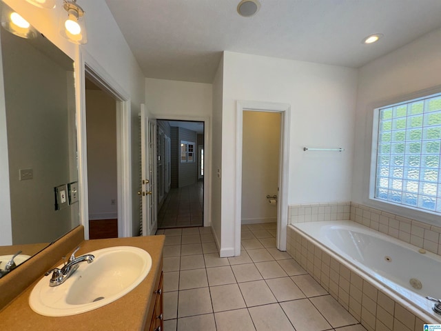 bathroom with a relaxing tiled tub, vanity, and tile patterned flooring