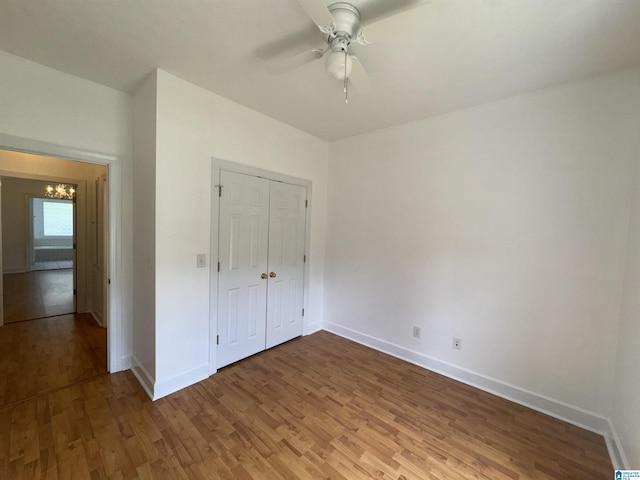 unfurnished bedroom with baseboards, a closet, ceiling fan with notable chandelier, and light wood-type flooring