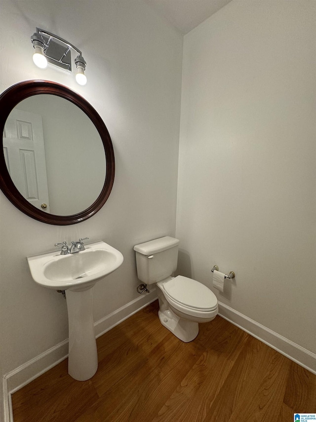 half bathroom featuring wood finished floors, toilet, and baseboards