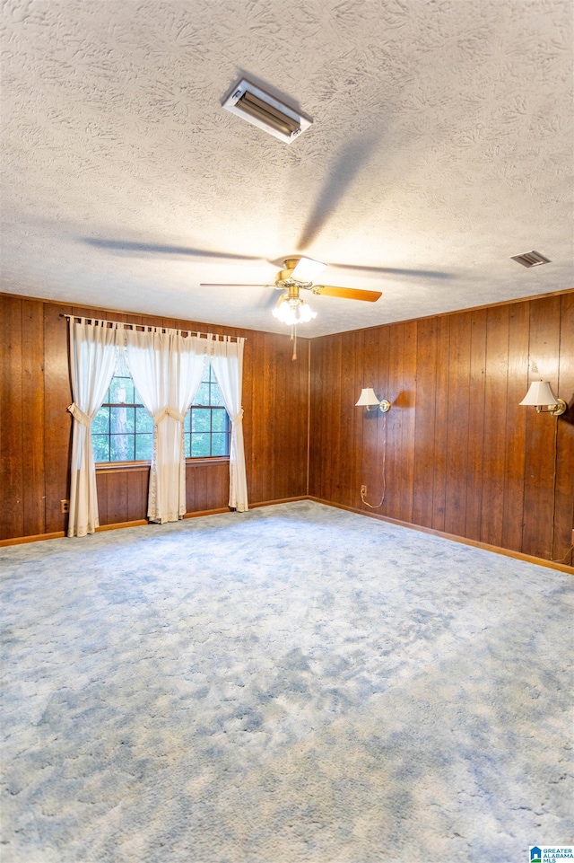 carpeted spare room featuring a textured ceiling, ceiling fan, and wood walls