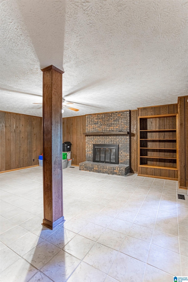 unfurnished living room featuring a fireplace, a textured ceiling, ceiling fan, and wooden walls