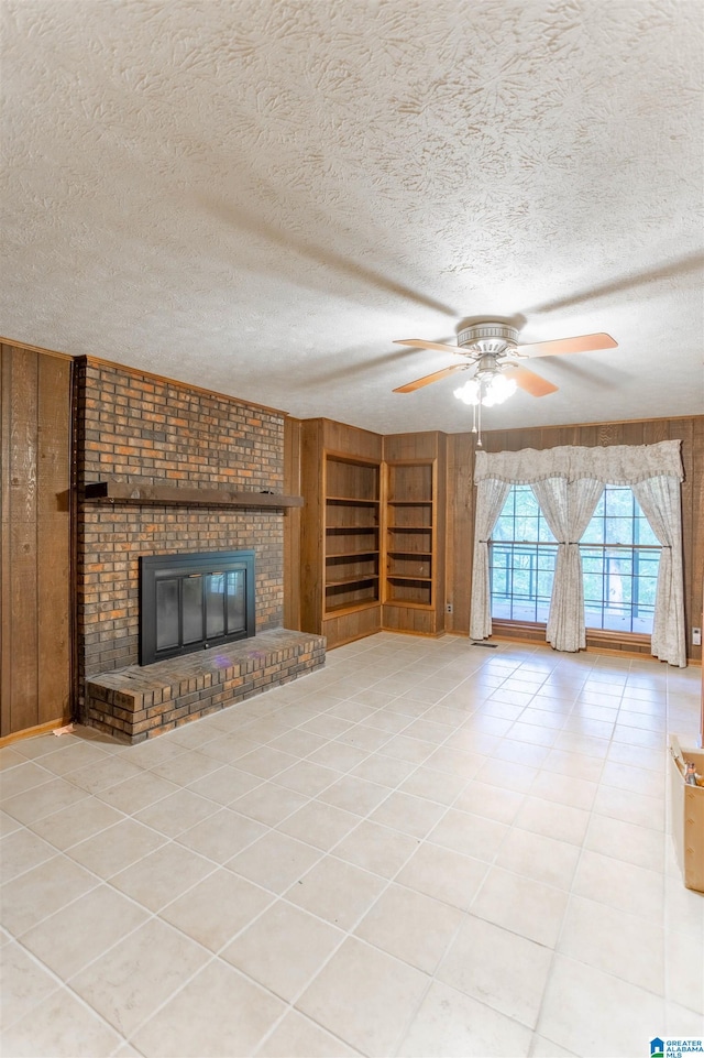 unfurnished living room featuring a textured ceiling, ceiling fan, wooden walls, and a fireplace