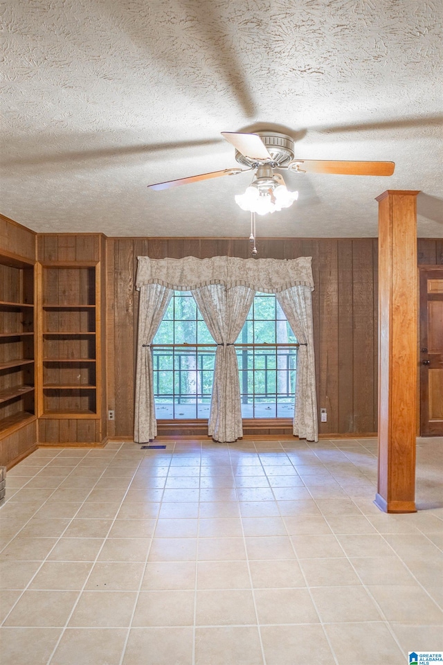 unfurnished room with built in shelves, tile patterned floors, a textured ceiling, wood walls, and ceiling fan