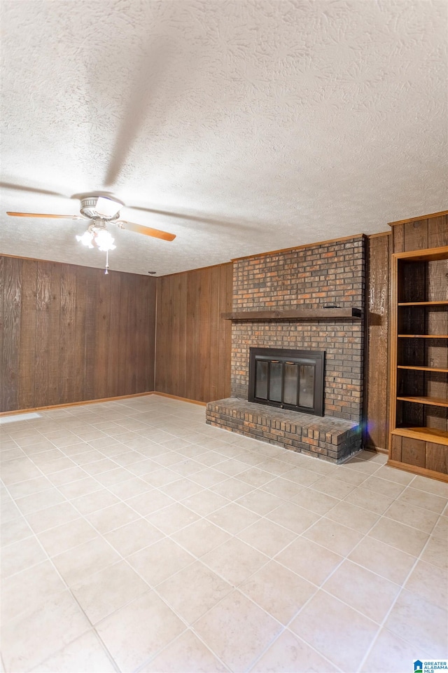 unfurnished living room with wooden walls, a brick fireplace, built in features, ceiling fan, and a textured ceiling