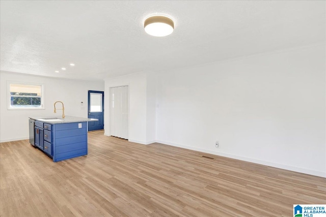 kitchen with an island with sink, blue cabinetry, sink, and light hardwood / wood-style flooring