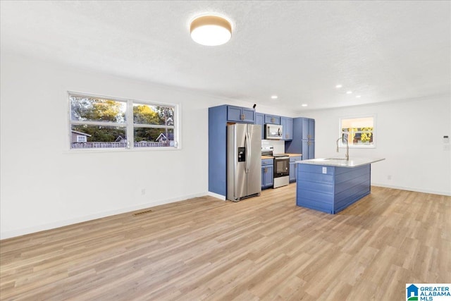 kitchen with light hardwood / wood-style floors, blue cabinets, sink, a kitchen island with sink, and appliances with stainless steel finishes