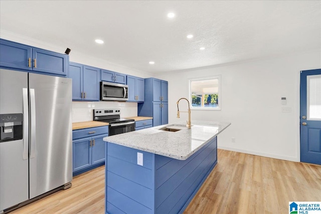 kitchen with sink, appliances with stainless steel finishes, light stone countertops, an island with sink, and light hardwood / wood-style flooring