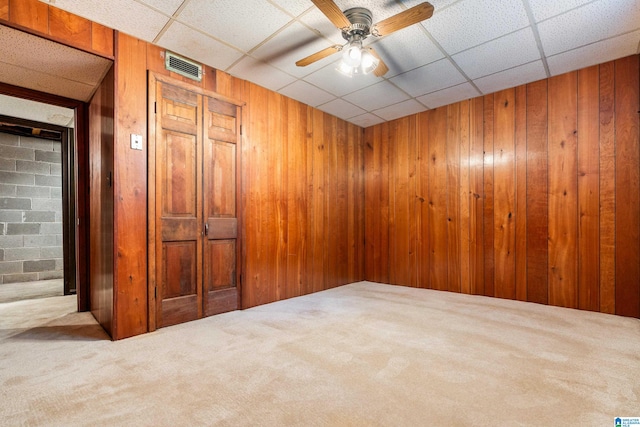 empty room featuring ceiling fan, wood walls, a paneled ceiling, and carpet flooring