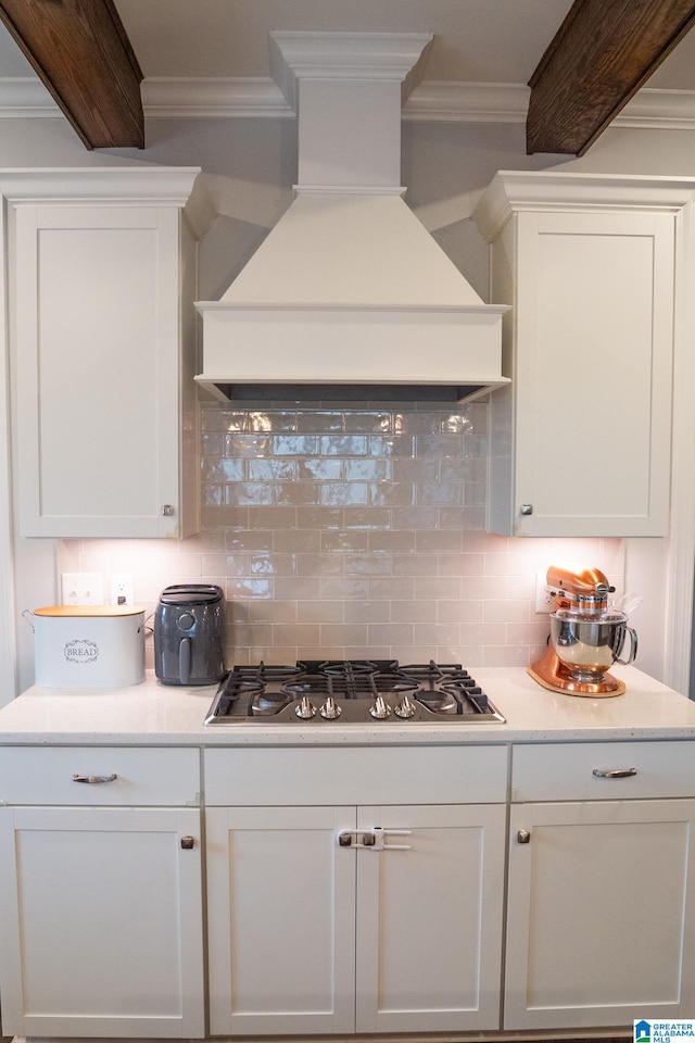 kitchen featuring crown molding, custom range hood, tasteful backsplash, white cabinetry, and stainless steel gas cooktop