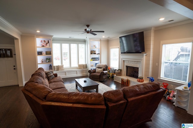 living room featuring built in shelves, ceiling fan, dark hardwood / wood-style flooring, crown molding, and a fireplace