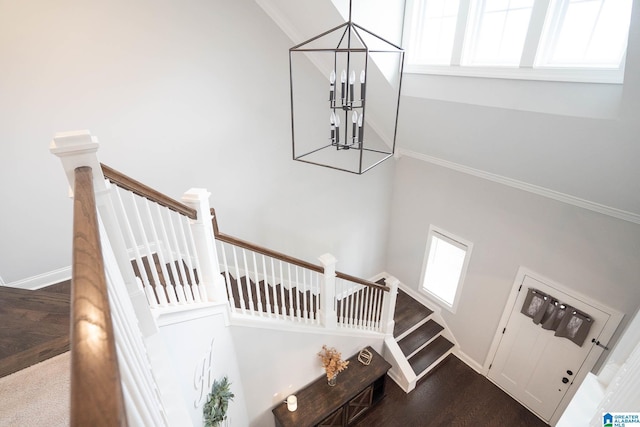 staircase featuring hardwood / wood-style flooring, crown molding, a high ceiling, and a notable chandelier