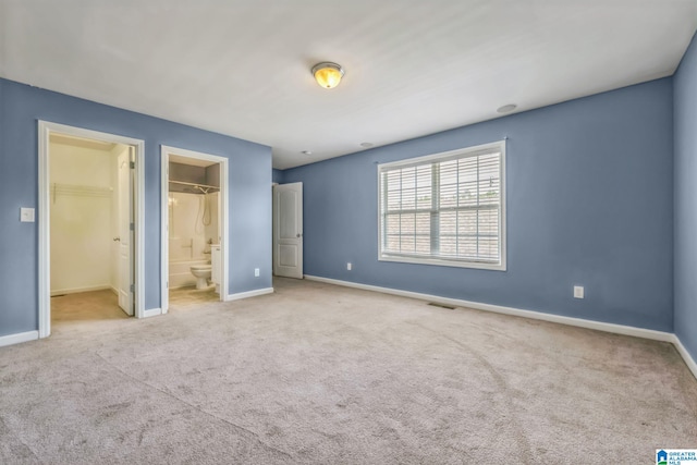 unfurnished bedroom featuring a closet, connected bathroom, a spacious closet, and light carpet