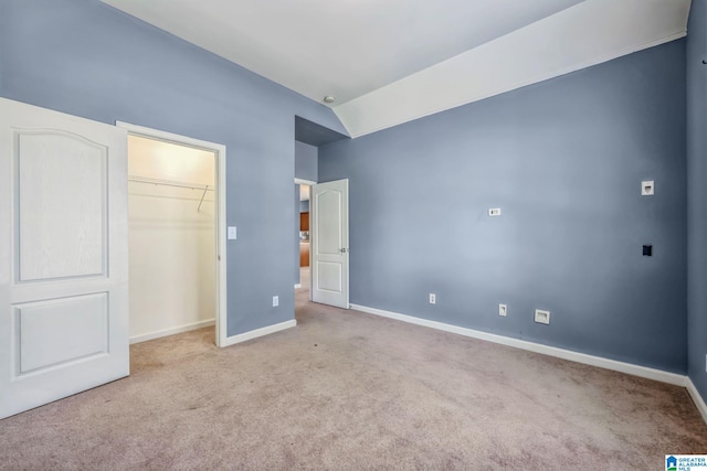 unfurnished bedroom with lofted ceiling, a walk in closet, and light colored carpet