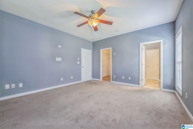 unfurnished bedroom featuring ceiling fan, a spacious closet, light carpet, and connected bathroom