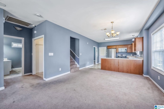 kitchen featuring decorative light fixtures, kitchen peninsula, an inviting chandelier, appliances with stainless steel finishes, and light colored carpet