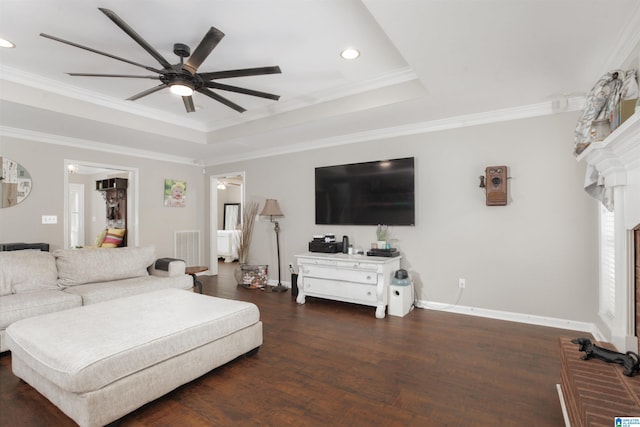 living room with a tray ceiling, dark wood-type flooring, a brick fireplace, crown molding, and ceiling fan