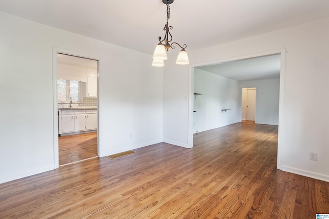 unfurnished room with light hardwood / wood-style flooring, a chandelier, and sink