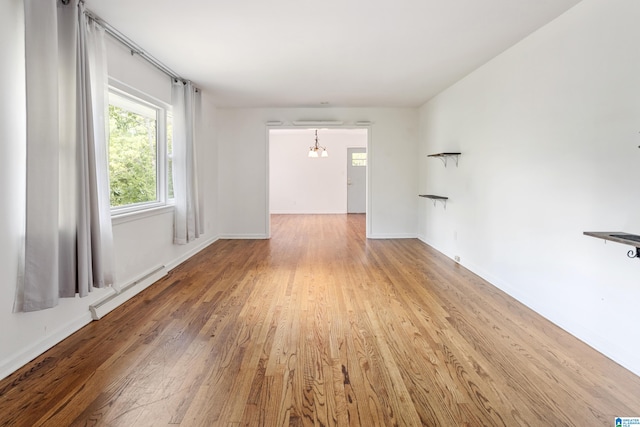 spare room with hardwood / wood-style floors, a chandelier, and a baseboard heating unit