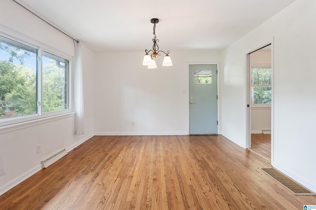 unfurnished room with baseboard heating, a notable chandelier, and light hardwood / wood-style floors