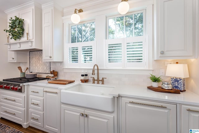 kitchen featuring decorative light fixtures, stainless steel gas stovetop, ornamental molding, sink, and white cabinets