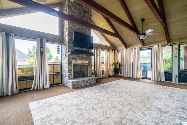 unfurnished living room featuring a stone fireplace, beamed ceiling, light colored carpet, and plenty of natural light