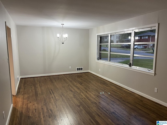 spare room featuring dark wood-type flooring and a chandelier