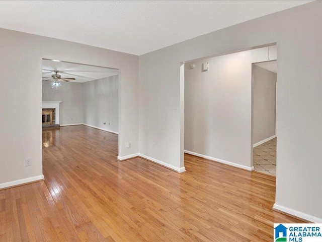 empty room with a fireplace, ceiling fan, and light hardwood / wood-style floors