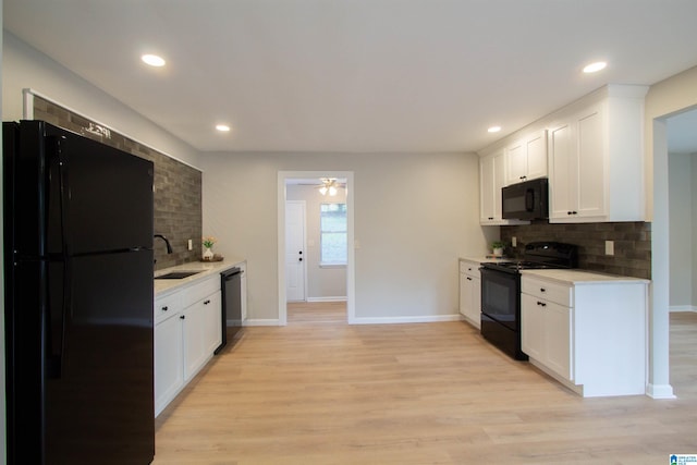 kitchen with light hardwood / wood-style flooring, backsplash, black appliances, sink, and white cabinets