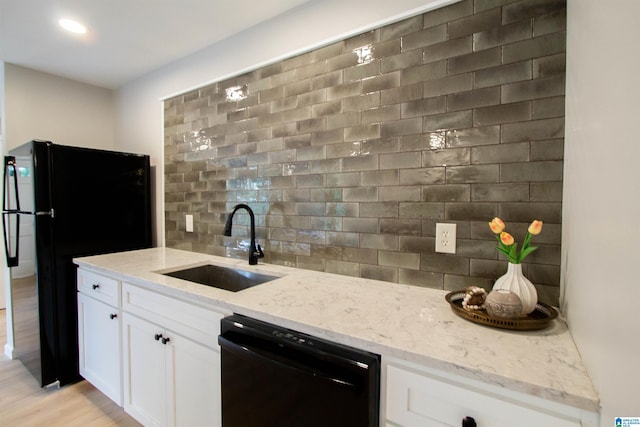 kitchen featuring light stone countertops, a sink, decorative backsplash, black appliances, and white cabinets