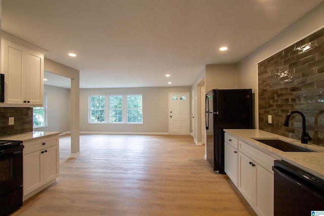kitchen with light wood finished floors, backsplash, black appliances, and a sink