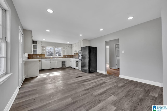 kitchen featuring sink, black fridge, backsplash, white cabinets, and hardwood / wood-style flooring