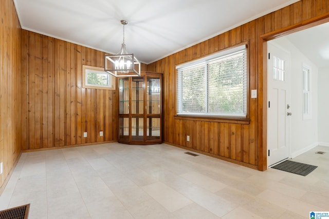 unfurnished dining area with crown molding, wooden walls, and a notable chandelier