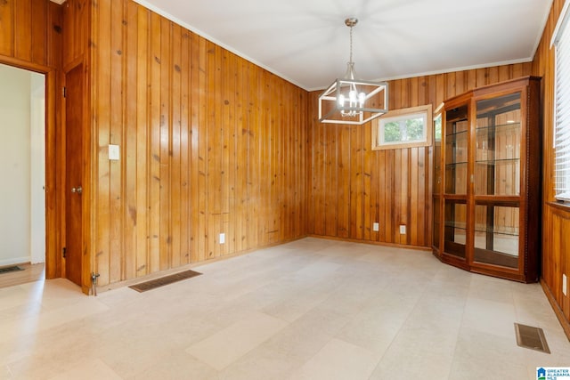 unfurnished dining area featuring ornamental molding, a notable chandelier, and wooden walls